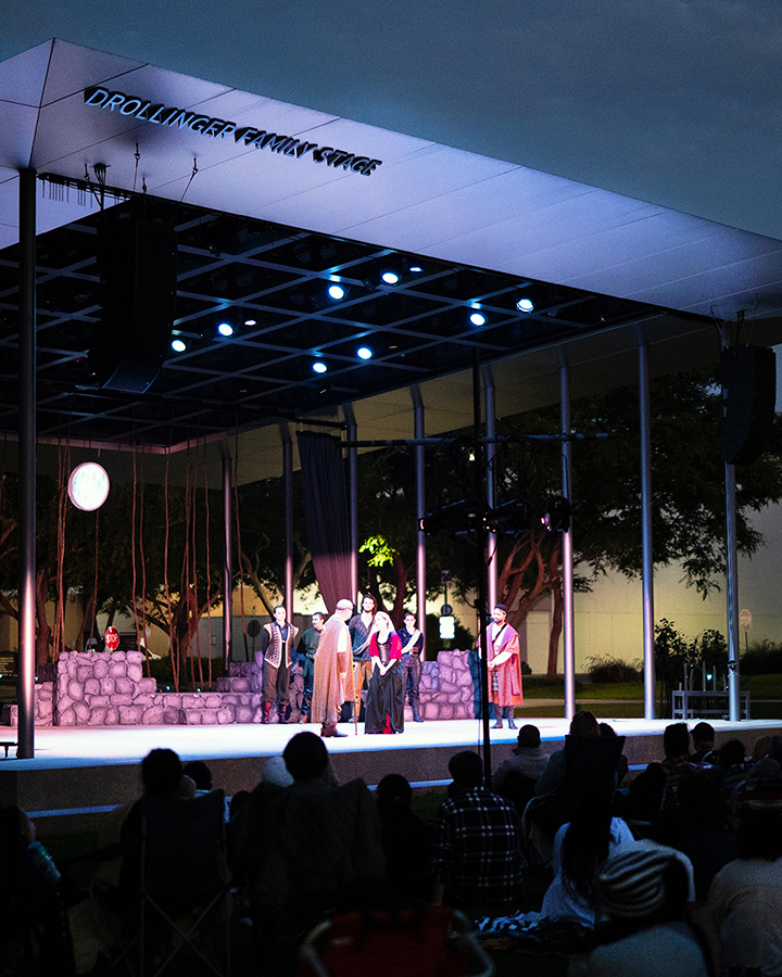 An outdoor theatre performance on a stage with a large audience at night